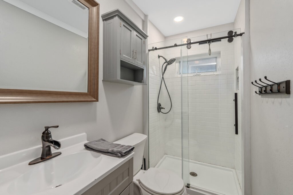 Standing shower with white subway tile and bronze removable hand-held shower head in custom bathroom.