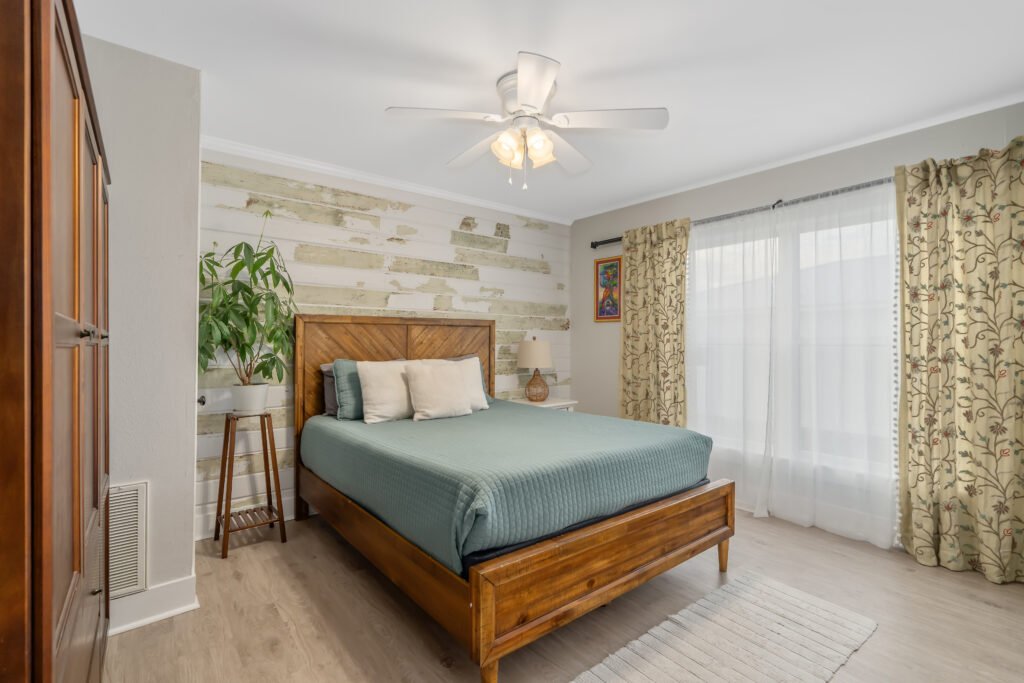 Custom hand-scraped shiplap wall gives character to well lit bedroom with large window, queen bed and armoir.