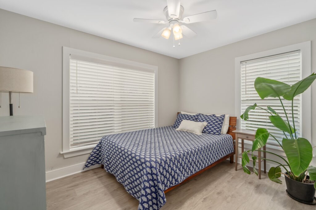Queen bed and potted bird of paradise tropical plant in 3rd bedroom of cozy bay cottage.
