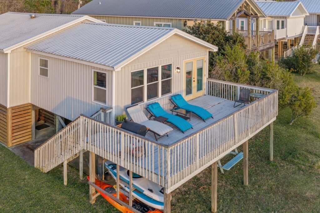 Sunbathing recliners on back porch of waterfront cottage with paddle boards and a kayak stored beneath.