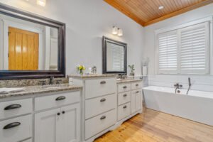 Luxurious master bathroom includes extra-deep soaking bathtub and separate shower over knotty pine wood flooring.