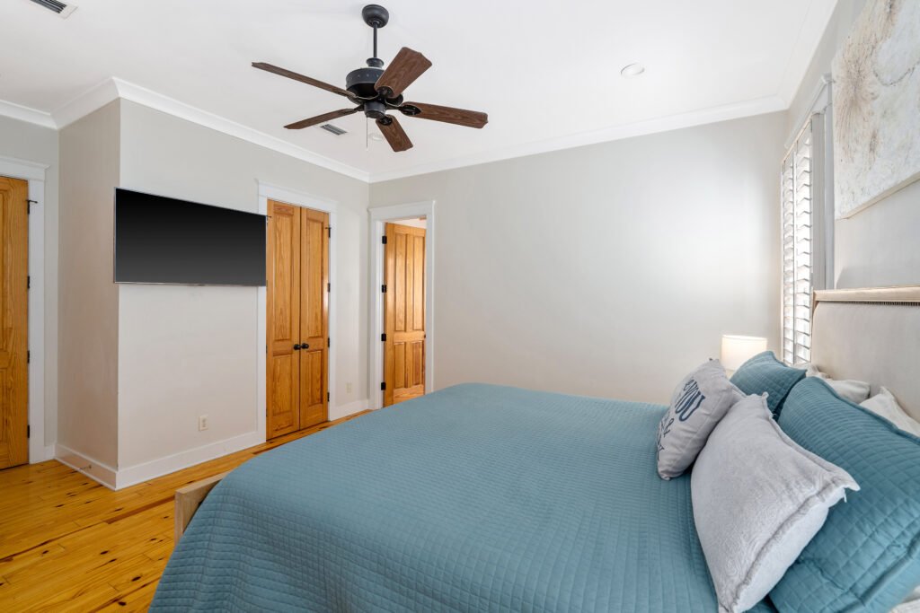 Master bedroom showing wall-mounted TV, walk-in closet , ceiling fan and door leading to master bathroom.