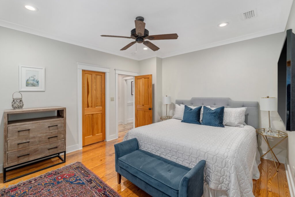 Upstairs bedroom with finished knotty pine wood floors shows king bed, wall mount television and dresser.