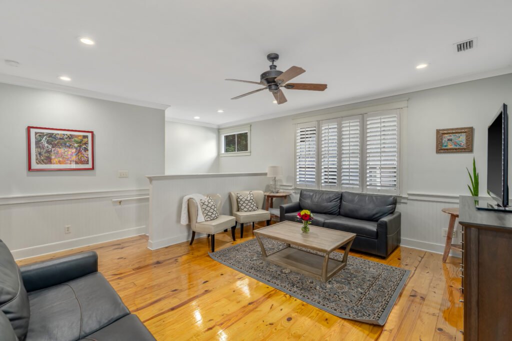 Secondary bedroom located upstairs has two black leather sleeper sofas and coffee table, knottyh pine wood floors.