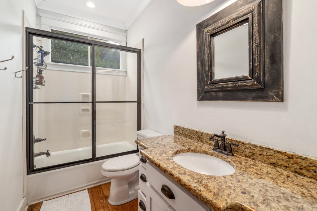 Full bathroom with granite vanity and full tub shower combination shows bronze fixtures and glass shower door.