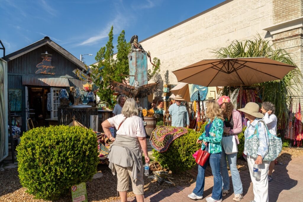 Art lovers browse a courtyard display featuring a bronze eagle sculpture and textile art near downtown Fairhope galleries during the Fairhope Arts and Crafts Festival 2026