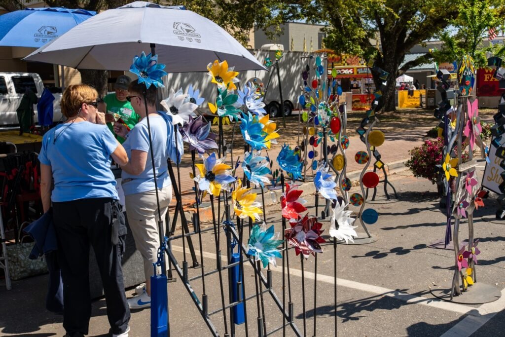 Festival attendees browse colorful metal pinwheel and windmill garden sculptures at a vendor booth during the Fairhope Arts and Crafts Festival 2026